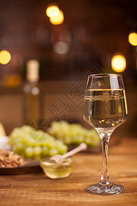 一杯白葡萄酒 旁边是一碗甜美的蜂蜜 在木制桌上坚果美食食物盘子水果玻璃饮料拼盘核桃酒杯图片