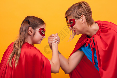 英雄花母亲和女儿穿得像超级英雄一样 玩手臂花管家庭戏服父母想像力童年航班游戏自由拥抱喜悦背景