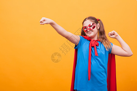 穿着超级英雄服装的小女孩在黄色背景上肖像优胜者幸福游戏乐趣戏服英雄童年蓝色飞行女性图片
