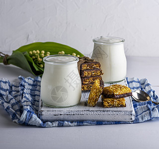 在玻璃罐子和零食中自制酸奶桌子蓝色饮食奶油勺子奶制品营养木头白色木板图片