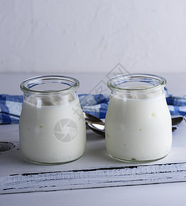 白木板上一个玻璃罐子中的自制酸奶奶制品桌子餐巾白色早餐勺子食物蓝色木头奶油图片