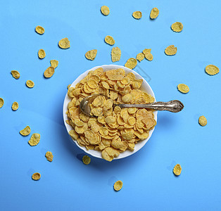 白陶瓷板和铁勺中的玉米片美食玉米黄色食物蓝色营养小吃勺子白色早餐图片