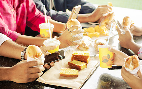 一群吃零食 忙着玩手机的人一起坐在大学餐厅 — 朋友们享受晚餐 快乐会议或吃垃圾食品并在吃饭时使用手机的概念图片