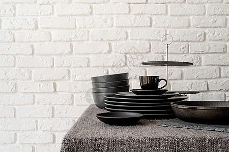 白砖墙底桌边的黑陶瓷盘和餐具堆叠件用具烹饪制品陶瓷杯子工具环境用餐厨具陶器图片