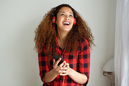 卷发的年轻女性戴着耳机和手机听音乐图片