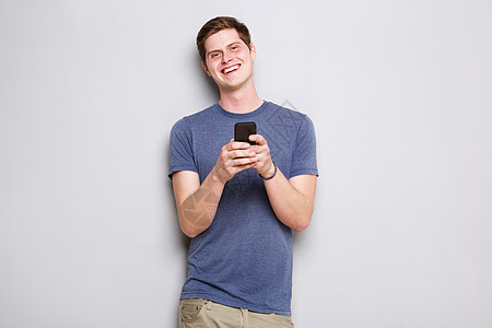 快乐的年轻人站在墙边 用手机站着图片