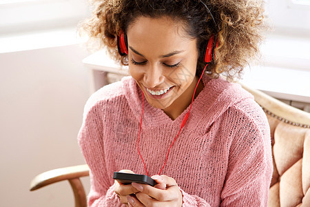年轻的非洲裔美国女性看着手机 戴着耳机听音乐图片