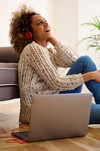 坐在家中用耳机和笔记本电脑监听音乐的黑人年轻妇女图片
