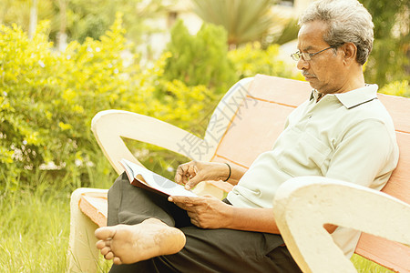 70 年代末看起来健康的老人坐在家里的花园里 在户外读书 — 老人在公园里认真读书放松图片
