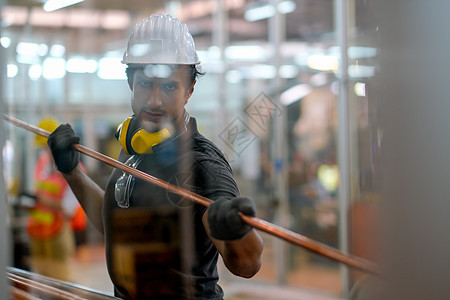 技术员或工人男子持有铜管 从工厂的玻璃窗中查看图片