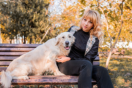 金金色的caucasians 女人坐在她的黄金拉布拉多猎犬 在公园的长椅上女子女孩犬类公共公园树叶种族女士猎犬朋友小狗图片