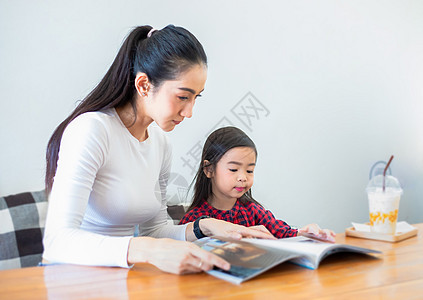 一位亚裔妈妈在客厅的桌子上教女儿在学期假期看书 家里的桌子上放着冷牛奶 家庭的教育理念和活动阅读作业教学父母母性孩子摄影沙发父亲图片