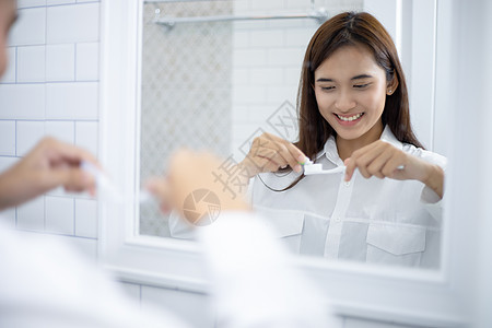 亚裔妇女挤着牙膏和刷牙 在刷子打扫卫生成人牙刷男人镜子洗涤母亲孩子图片