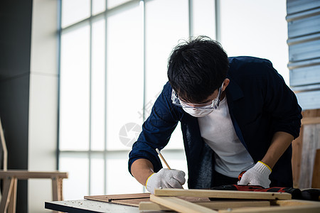 亚洲男木匠在家里用木工工具和木头在车间里处理技术图纸或蓝图建筑纸工人工艺男人工作项目工匠木材小屋桌子职业图片