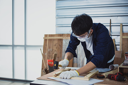 亚洲男木匠在家里用木工工具和木头在车间里处理技术图纸或蓝图建筑纸木板制作者工艺工匠工作职业男性房子作坊男人图片