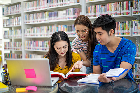 亚洲组学生团体 微笑和阅读书及使用笔记本多样性项目书架图书馆教育青年电脑女士教科书桌子图片