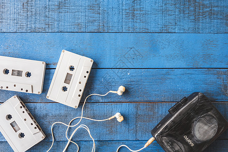 Cassette 播放器的顶部视图 其音频带在蓝色木制表格背景上纽扣录音带卷轴播送塑料磁带娱乐玩家音乐记录图片