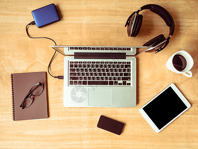 木桌背景上带有笔记本眼镜和咖啡杯的电子设备的顶部视图图片