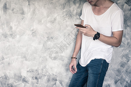 青年男子穿着白色T恤衫和蓝色牛仔裤 手持智能电话 站在灰红色的老乡背景上棉布衬衫牛仔布衣服男性空白潮人男人身体裤子图片
