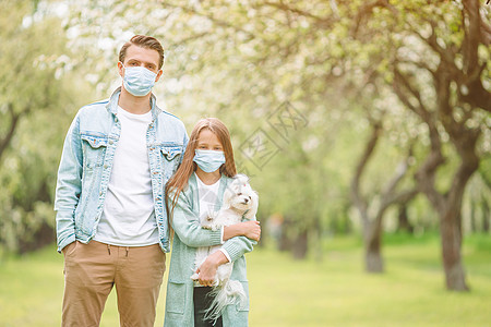 狗生病父亲和女儿家庭在盛开的樱花花园中戴面罩自由细菌女孩园艺口罩父母母亲药品面具感染背景