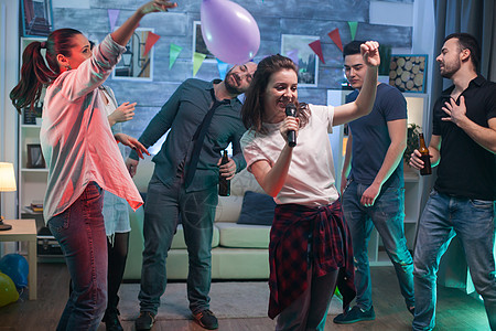 在派对上唱卡拉OK的 兴奋的年轻女子歌曲唱歌伙计们气球酒精音乐麦克风沙发乐趣朋友们图片