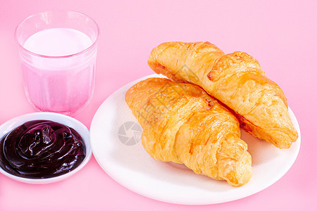 白色盘子上两个羊角面包和粉红背景的新鲜牛奶杯脆皮咖啡店巧克力糕点玻璃美食早餐奶油营养咖啡图片