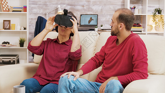 侄女教他祖母如何使用VR护目镜女士帮助娱乐模拟耳机惊愕家庭沙发房间眼镜图片