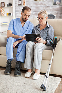 在养老院有拐杖的老年妇女护理女士药片微笑帮助疗养院电脑照顾者助手访问图片