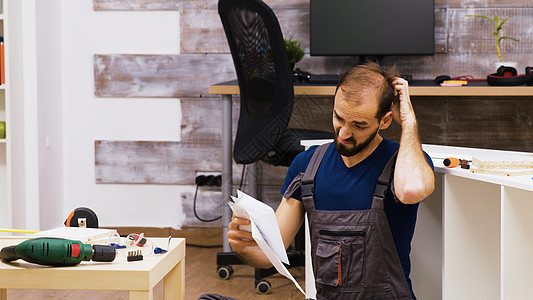 工人在阅读新家具教学时 用困惑的工人摩擦他的头部工具承包商公寓木头架子工作房子螺丝刀客厅工匠图片