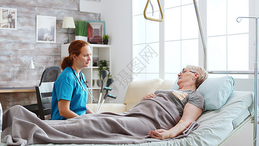 退休养老院护士与躺在医院床上的一位老妇人交谈治疗成人说谎男性男人老年病房女士医生药品图片