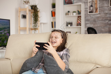 快乐的小女孩玩智能手机游戏游戏电话长椅短信说谎女学生沙发女性青春期细胞女士图片