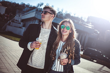 在街上散步喝鸡尾酒 玩得开心的情侣快乐幸福男性夫妻街道喜悦帽子太阳镜果汁玻璃图片