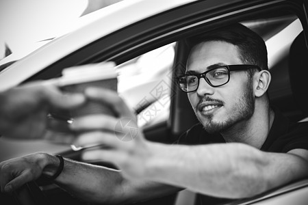 年轻笑笑的男子驾驶汽车和喝咖啡图片
