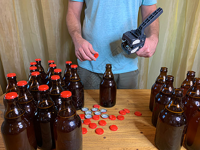 在家酿造的手工艺啤酒 男人特写棕色玻璃啤酒瓶 用红色冠盖在木制桌上的塑料罩子草稿橙子机器啤酒厂金属酿酒师补给品盖帽工艺液体图片