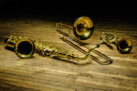 黄色黄铜管乐器 — 萨克斯管 长号 带背光的木制舞台上的小号图片