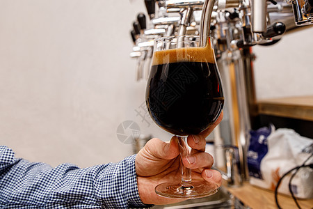 酒保在酒吧里从水龙头上倒新的黑啤酒啤酒调酒师啤酒厂泡沫餐厅服务酒精食物酿造工艺图片