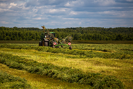 暴风雨前夏季田野上的绿色干草拖拉机  具有选择性聚焦和模糊的长焦镜头环境国家收获农业收成农田机械车工金属工具图片