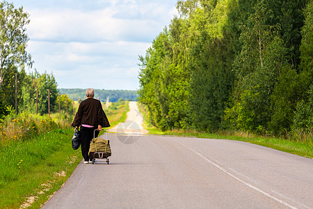 在阴云的夏日 带马车和黑色塑料袋的老女人在古老道路边上走图片