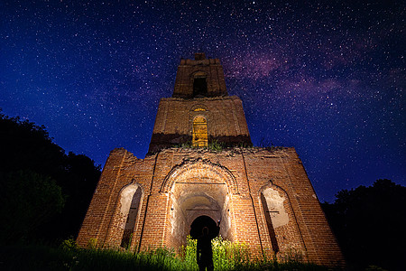 星星火炬夜钟塔在星夜的森林中废墟 而手电筒下的男人背景