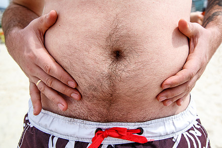 一个肥胖的胖子在沙滩上露出肚子图片