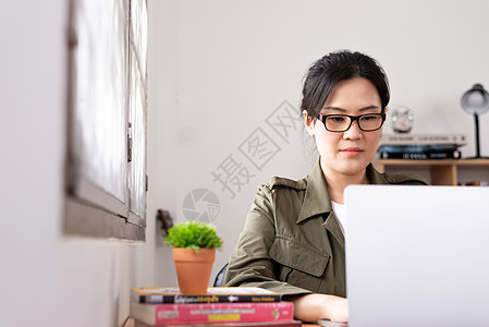 现代亚洲年轻女性在家工作 笑声窗户眼镜桌子笔记本商务书架房子咖啡职场房间图片