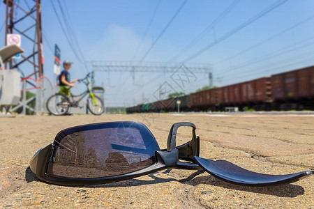 在男孩骑自行车和行驶的火车经过的背景下 破碎的眼镜躺在火车站图片