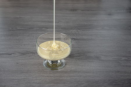 以木制背景的透明玻璃碗中冷凝牛奶勺子甜点桌子奶制品茶匙沙锅烹饪食物漩涡厨房图片