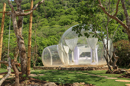 带有透明墙壁的浪漫泡泡屋 白色木制双人床 泡沫内有蚊帐 在充气帐篷里度蜜月 印度尼西亚巴厘岛热带天堂的旅游胜地图片