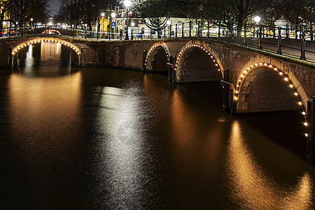 夜间在阿姆斯特丹平静的运河水面上反射出灯火通明的阿姆斯特丹运河桥图片