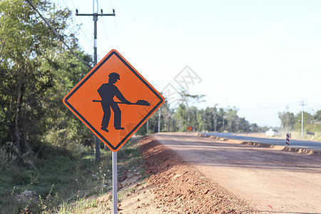 橙色标志显示了一个符号 上面有一个人拿着铲子的图像 在安装在施工道路一侧的标志上 指示道路施工的警告标志在前面图片