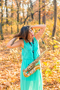 穿着长蓝色长裙和高空萨克斯风的深褐发美女 在黄色秋天公园装扮背景图片