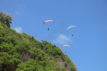 在天空中滑翔伞 三架单人滑翔伞在夏日飞越热带巴厘岛 美丽的滑翔伞在绿松石色的背景下飞行 积极的生活方式和极限运动的概念冒险肾上腺图片