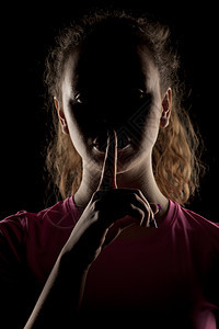 女人的脸在阴暗中 用手指指着她的嘴唇戏剧性灯光女性无名手势肩膀女孩阴影卷发照片图片