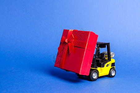 黄色叉车运载一个带蝴蝶结的红色礼盒 购买和交付礼物 零售 折扣和竞赛 比赛促销 增加销售额并吸引新客户背景图片